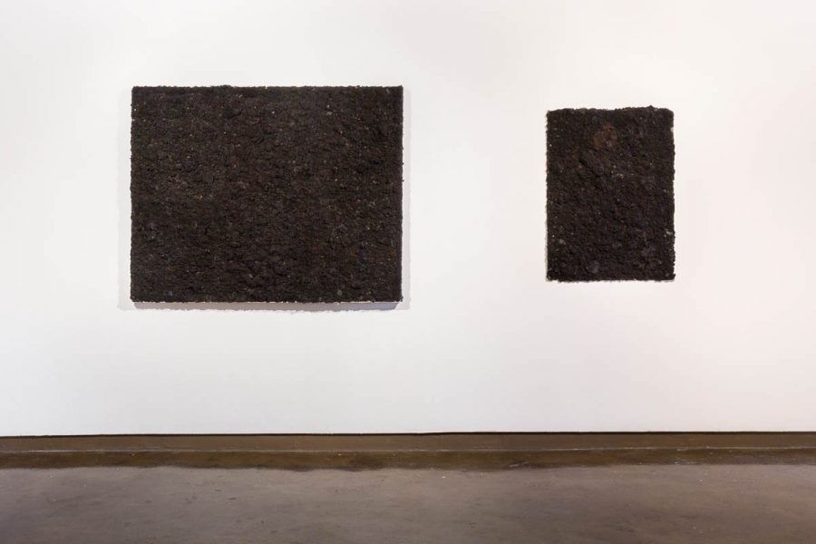 Two artworks by Ade Bunmi Gbadebo hanging on a wall. The work features human hair that was collected from barber shops that have been sewn onto a canvas.