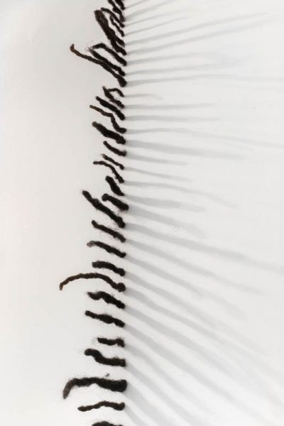 A vertical array as a column installed on a wall with pieces of human hair