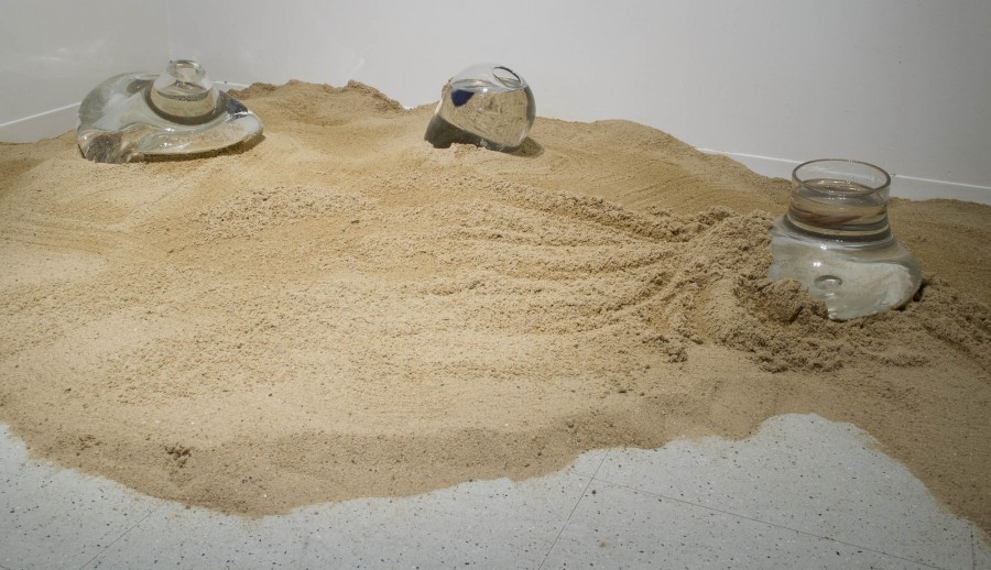 Installation of sand and 3 curved glass objects displayed on the floor.