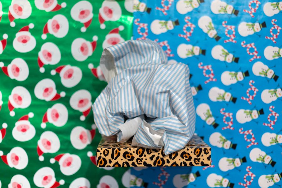 A sculpture made of organic fabric material with white and blue strips patterns, on an animal print pattern material, and behind are installed two present wraps sheets, one with a Santa Claus head on a green background, and the other one is with snowmen and candy canes on blue background