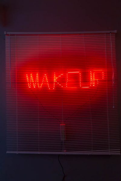 A red neon light with the WAKEUP shape is installed on a window under window blinds, and it is illuminating