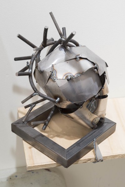 Sculpture of metal welded helmet from thin sheets of metal in front and thin metal bars shaped around the back of the head with blunt spikes.