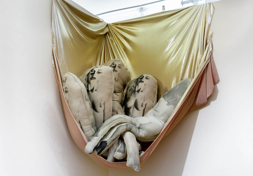 Silkscreen stuffed pillows with nude female print on them, sitting on a suspended golden cloth.