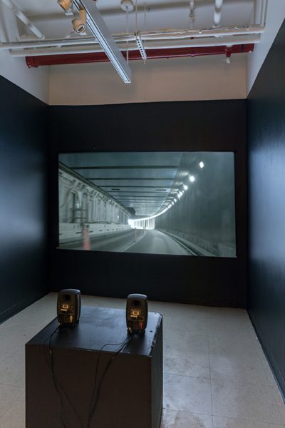 Installation view of artwork by Alexandra Russo. View of a video projection on a black wall of a tunnel used for automobile traffic.