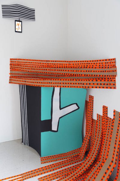 Installation view orange tapes blued on the floor and on the wall and turquoise shapes installed in the corner of the wall which has a white stripe with black outline on it