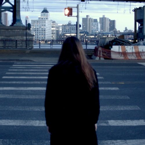 Artwork by Alexandra Russo. Still video image of a figure in front of a cityscape.