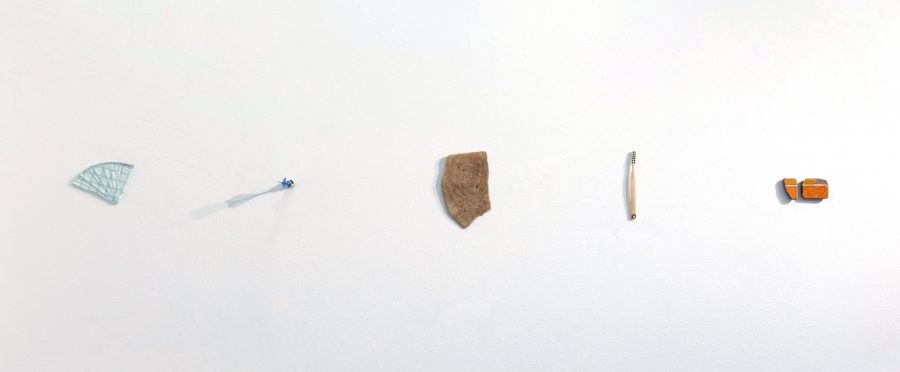 Five small fragments of objects installed on a white wall.