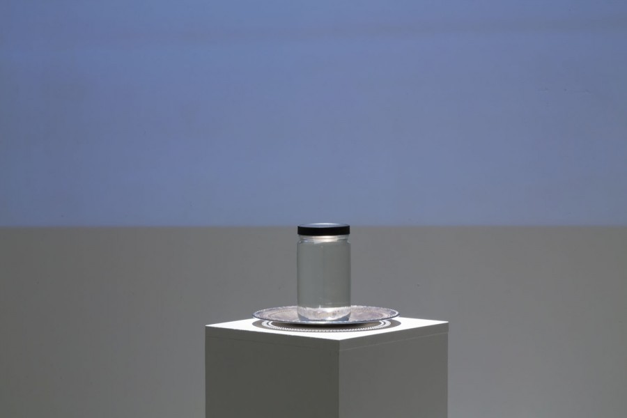 Installation of a sculpture representing a jar with a black lid closed on a plate put on a stand.