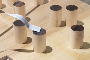 Detail of installation by Andrew Lee. Cylindrical wooden objects placed on a wooden surface.