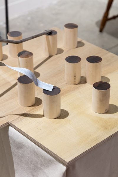 Detail of installation by Andrew Lee. Cylindrical wooden objects placed on a wooden surface.