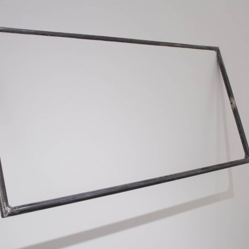 A view of a rectangle shape made of metal rods welded together and installed on the wall with the top part stuck on the wall, and the bottom part is at a distance from the wall