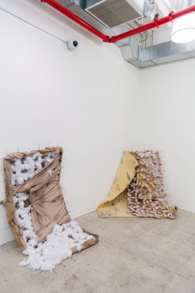 Installation view of sculptures made of silky fabric, with white fluffy organic material inside, supported by the wall