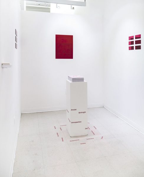Studio installation with a red painting mounted on the back wall and smaller red paintings on the left and right, with a pedestal in the center with red letters on the pedestal and floor.