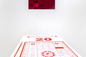 Red painting mounted on a wall in the background, a stack of red calendars in the foreground.