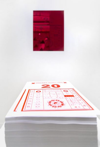 Red painting mounted on a wall in the background, a stack of red calendars in the foreground.