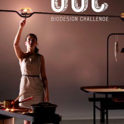 Poster with a woman wearing a white dress reaching up to a lightbulb with a table in front of her with two pots on it, "bdc biodesign challenge" is printed on the upper right of the poster