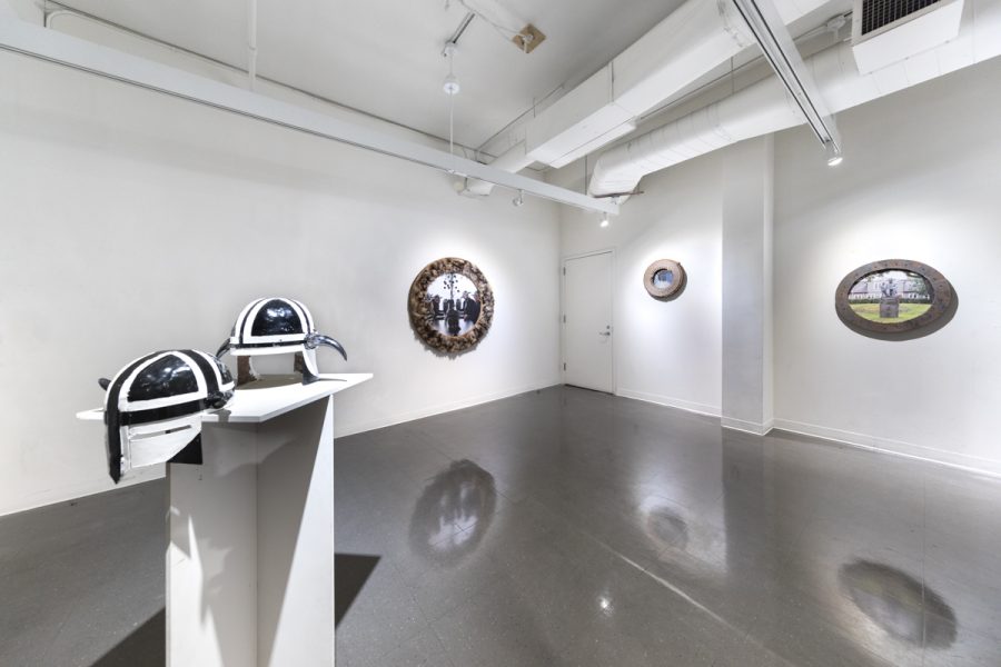 Installation view of artwork by Bjorgvin Jonsson. Multiple circular constructed frames with images of people wearing helmets. Two black and white helmets placed on a pedestal. 