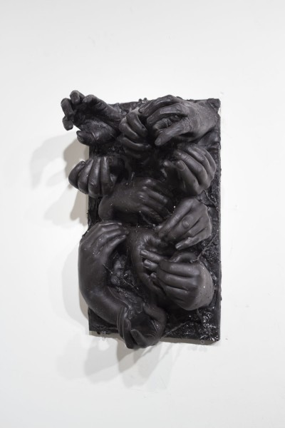 A sculpture made of a casted black material representing hands and fingers in various positions, the sculpture is mounted on the wall with screws