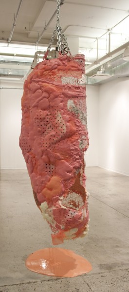 a sculpture made with organic shapes material hung on the ceiling with chains and mesh, orange-colored surface, and light orange paint dripping on the floor