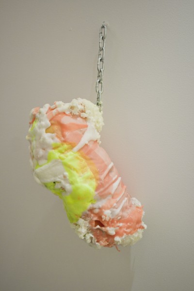 Organic-shaped sculpture colored with orange, white, and neon yellow hung on the wall with metal chains.