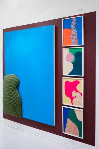 Installation view of an artwork made as a composite from geometrical shapes of organic fabrics in green, orange, pink, beige, glued on square frames with blue as the background, beige, or orange