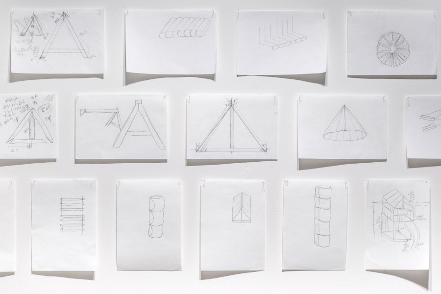 A grid of graphite drawings on the wall with different geomatical shapes like triangles, cones, cubes, etc.