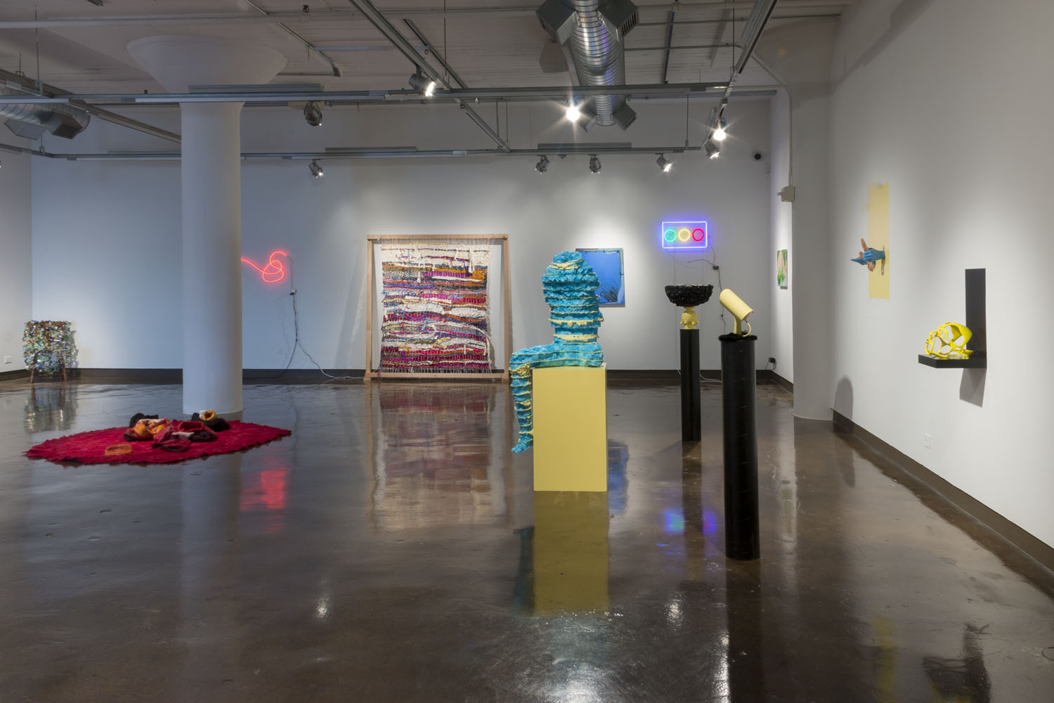 Installation view of blue anthropomorphic sculpture, a red rug with fabric pieces, and other objects.