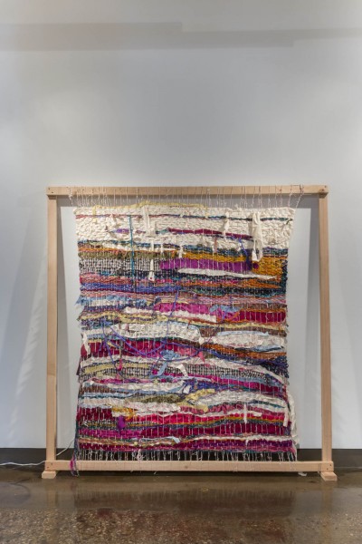 A close-up image of a multi-colored cloth made out of different pieces of colored fabrics. The piece is hung in a wooden frame.