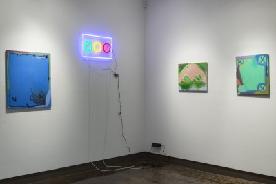 An installation view of artworks by Luke Lunsford. The view is of a corner of a room with three paintings and a neon light sculpture hanging on the wall.