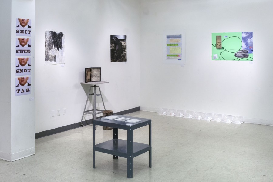 Installation view of prints, sculptures, and other media  installed on the wall, on stands, and a black table