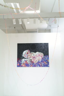 A colorful, abstract figurative painting hung against a white wall.