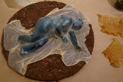 A close-up shot of a small 3-d print of a reclining female figure draped in dehydrated scoby.