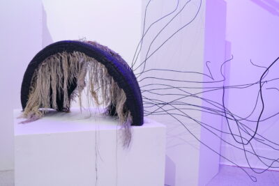 An abstract sculpture made with wires and a rubber tire sitting on a white pedestal.