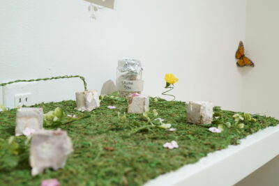A close-up view of small sculptures made of mycelium, arranged on top of a shelf covered in moss.
