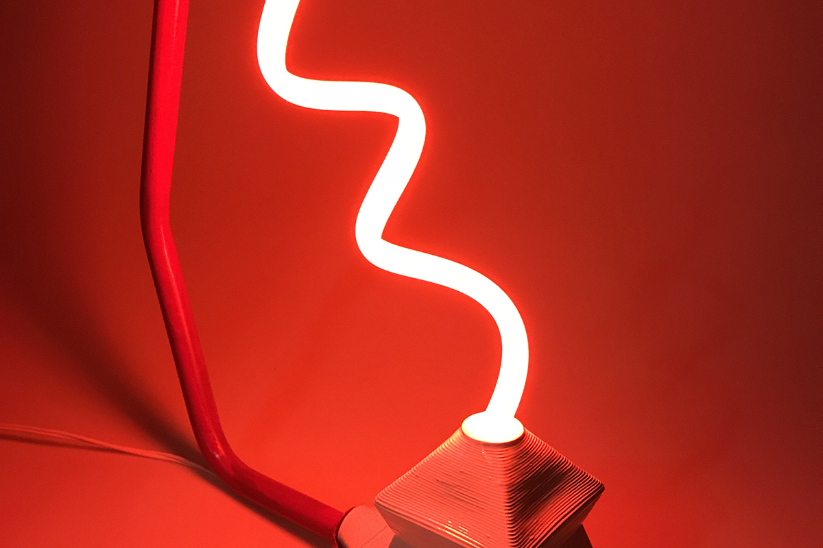 A sculpture by Dakin Platt. The sculpture is has a rod and base holding a thin twisted neon light. The color of the light is bright red. The background is a plain backdrop.