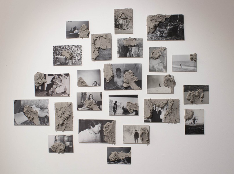 A view of multiple photographs on a wall. Photographs are in back and white, and they represent different persons and children, and some of the photographs have splashes of molded added on them to cover persons or to cover parts of the photograph.