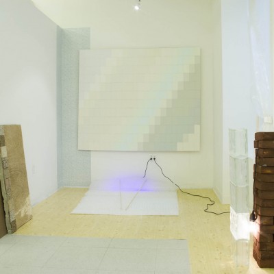Installation view of bubble wrap, neon light in the background, a large-scale canvas above it, and wood pieces and bricks.