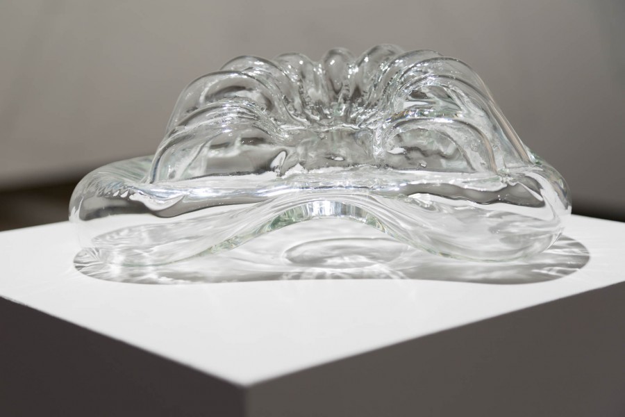 A close view of an organic-shaped sculpture made of glass and placed on a white stand.
