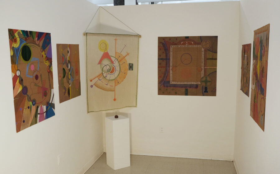 Installation shot of 5 pencil drawings of colorful geometric shapes and a silk tapestry