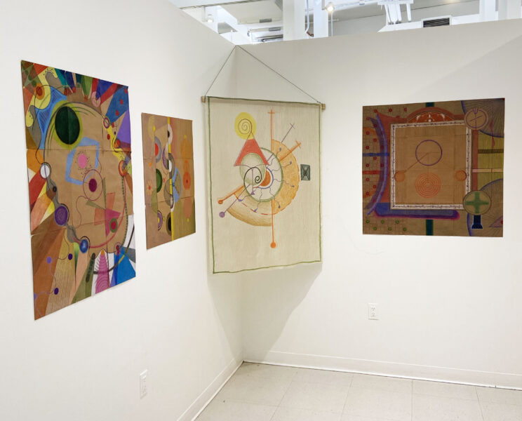 Installation shot of 3 pencil drawings of colorful geometric shapes and a silk tapestry