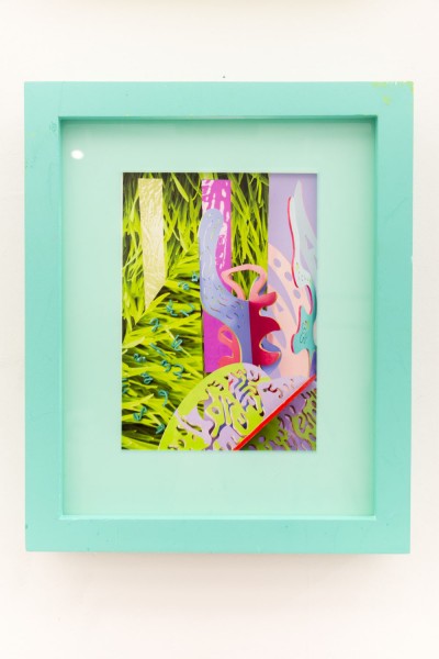 Abstract sculpture made with organic curved shapes, in green, bright pink, baby-blue, and violet installed in a turquoise frame and hung on the wall