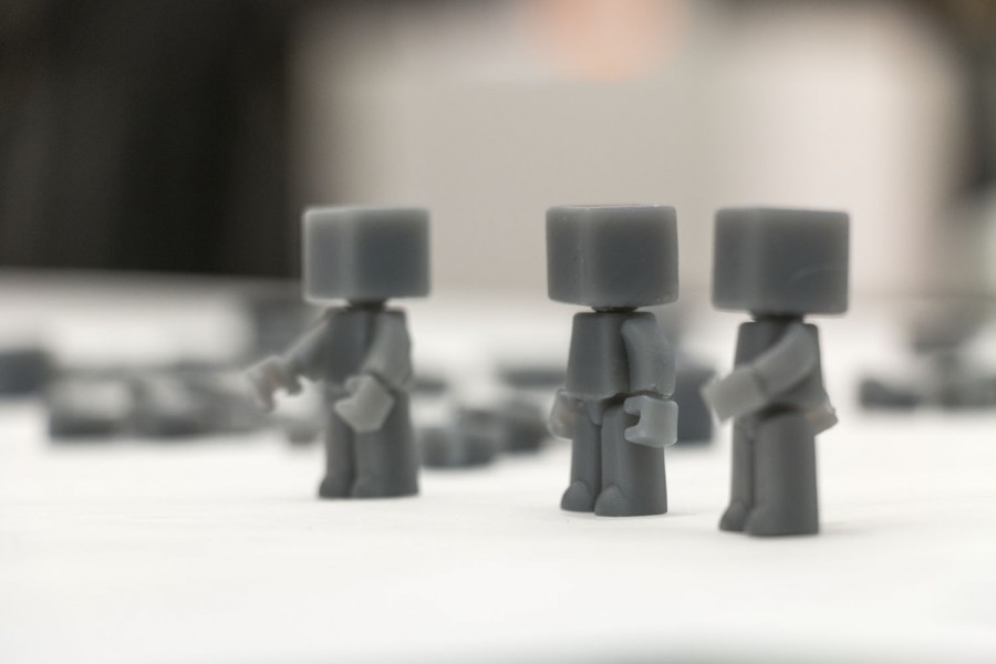 Black 3d-printed figurines with square heads and squared body parts placed on a white table