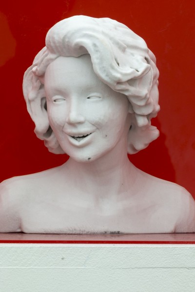 White bust sculpture of a woman with a prominent smile expression, head looking slightly to a side, and short hair