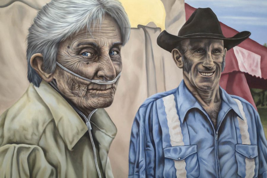 The painting represents two old men, one with white hair and a medical device under nouse, and a yellow shirt. The other one wears a blue shirt and a black hat and has a big smile on his face. In the back is a big tent with red and beige fabric