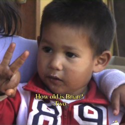 Screen capture from a clip of a boy OK sign with his hand and a caption: How old is Brian? and the answer: Two.
