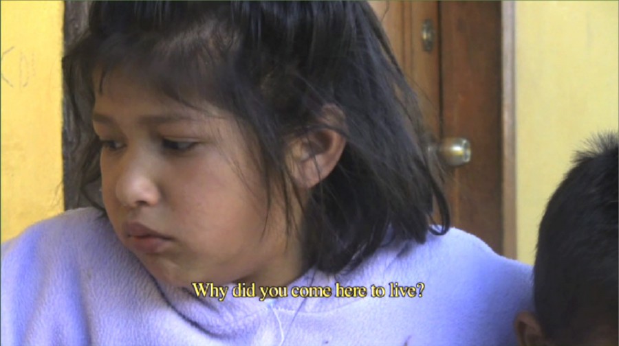 Screen capture from a clip of a girl looking away from the camera and a caption: Why did you come here to live?