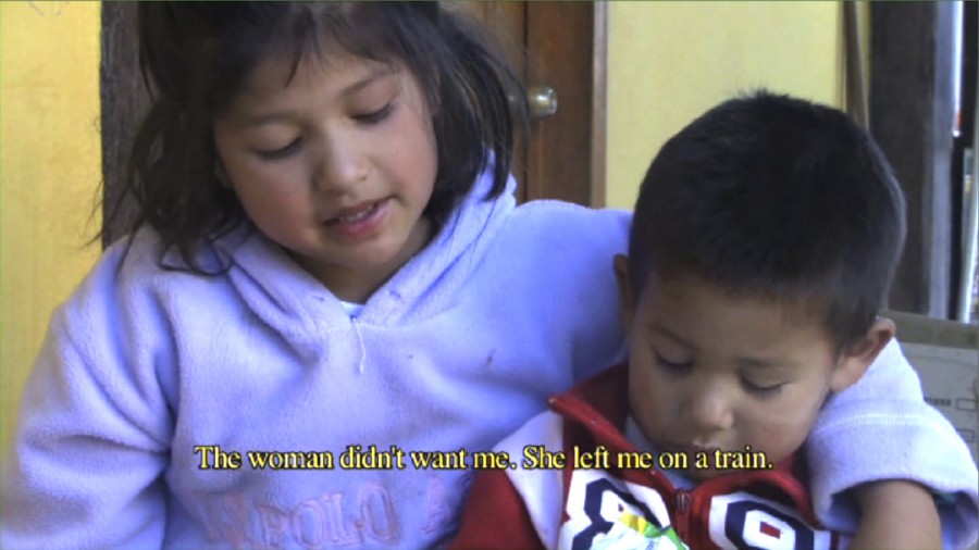 Screen capture from a clip of two children hugging and a caption: The woman didn't want me. She left me on a train.