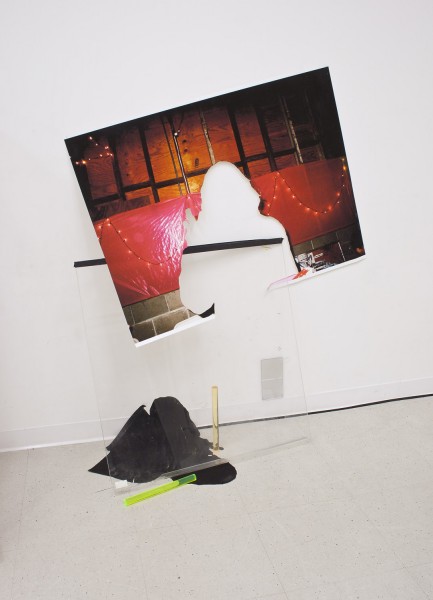 A print of a person with the person's shape cut-out in a room with a wooden wall and a red plastic strip with fairy lights as decor, installed on a white wall with a transparent plexiglass piece under it, a black piece of fabric, a neon green and a golden cylinder tube on the floor