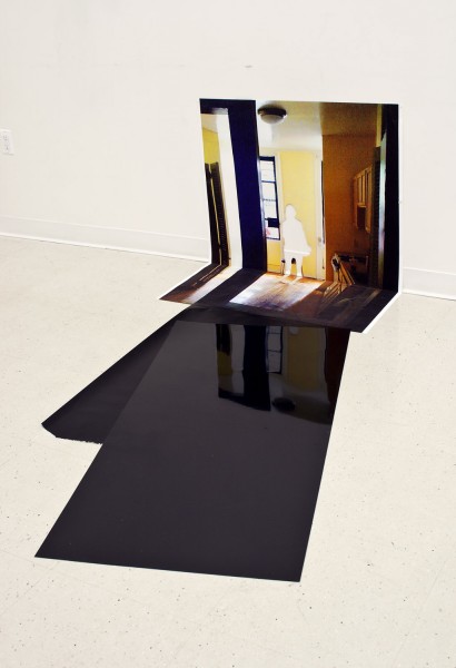 Painting of a white silhouette in a room with natural light and a reflective sheet of black material is placed at the bottom of the painting on the floor