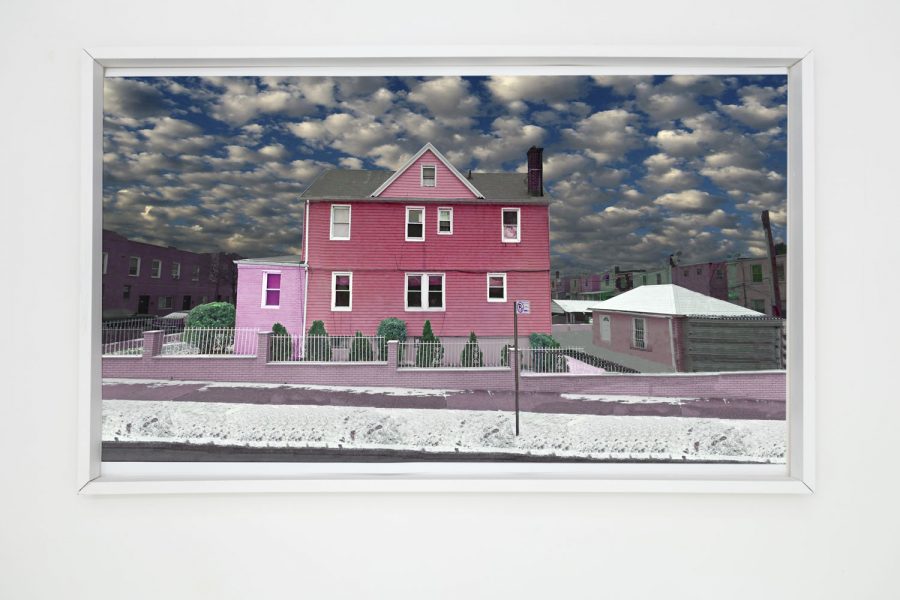 Photograph of a pink house in front of a blue sky with white clouds in a white frame.